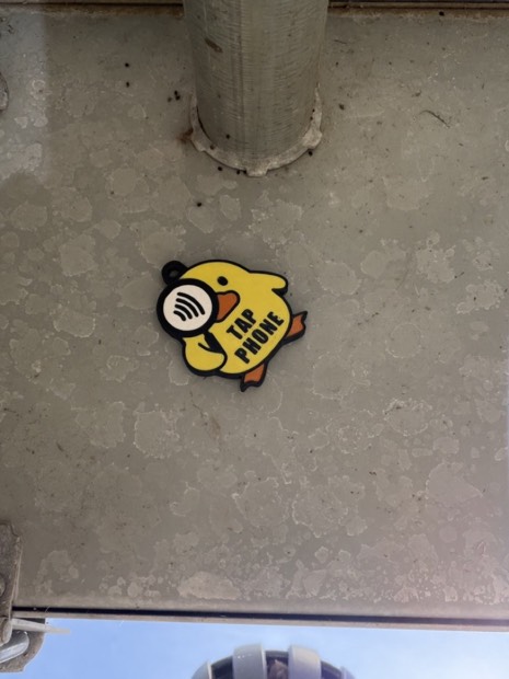 A yellow tap-phone duck tag resting on a concrete ledge