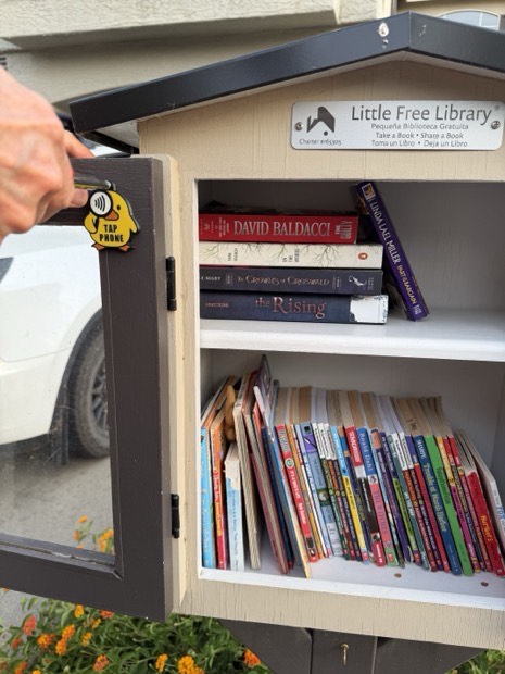 A duck tag on the open door of a Little Free Library